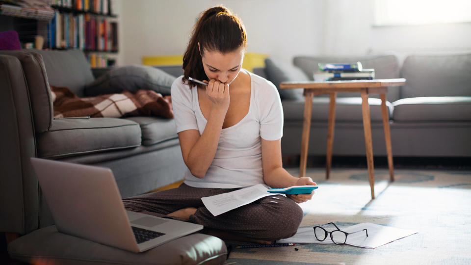 Photo of a young woman sitting on the floor and working on laptop.