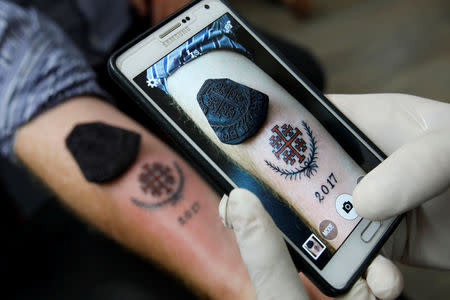 Tattoo artist, Wassim Razzouk, who is continuing his family's tradition of inking Christian pilgrims with ancient tattoos, takes a picture on a mobile phone showing an ancient wooden tattoo stamp displayed near a recently completed tattoo at his studio in Jerusalem's Old City November 27, 2017. REUTERS/Amir Cohen