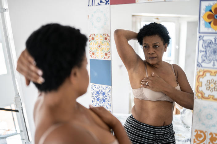 Une femme noire fait un auto-examen des seins à la maison.