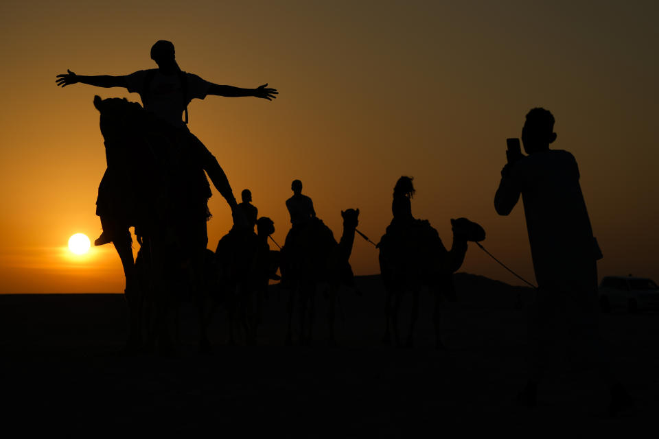 A man has his photo taken atop a camel in Mesaieed, Qatar, Nov. 26, 2022. Throngs of World Cup fans in Qatar looking for something to do between games are leaving Doha for a classic Gulf tourist experience: riding a camel in the desert. But the sudden rise in tourists is putting pressure on the animals, who have almost no time to rest between each ride. (AP Photo/Ashley Landis)