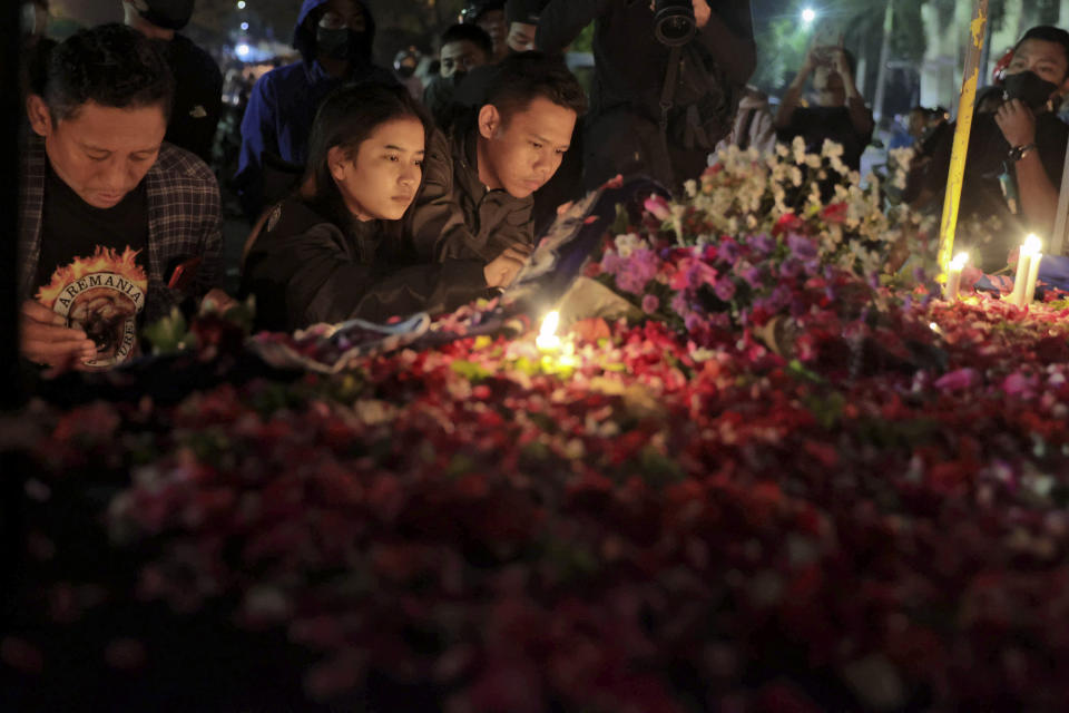 People lay flowers during a candle light vigil for the victims of Saturday's soccer riots outside Kanjuruhan Stadium where it broke out, in Malang, East Java, Indonesia, Sunday, Oct. 2, 2022. Police firing tear gas after an Indonesian soccer match in an attempt to stop violence triggered a disastrous crush of fans making a panicked, chaotic run for the exits, leaving a large number of people dead, most of them trampled upon or suffocated. (AP Photo/Trisnadi)