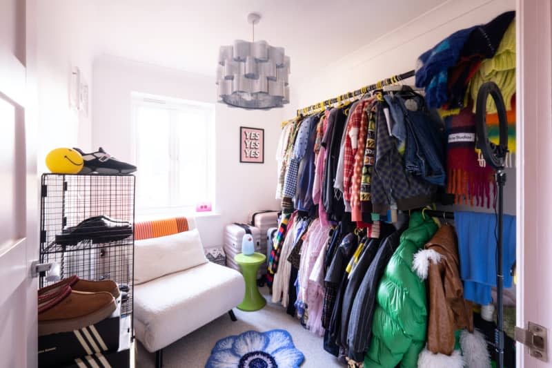 Clothing hangs from racks in white room.