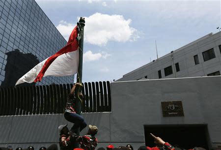 A protester climbs a pole to erect an Indonesian flag in front of the Australian embassy during a demonstration in Jakarta, November 21, 2013. Australia warned travellers to Indonesia of a planned demonstration at its embassy in Jakarta on Thursday as anger grows over reports Canberra spied on top Indonesians, including the president and his wife. REUTERS/Beawiharta