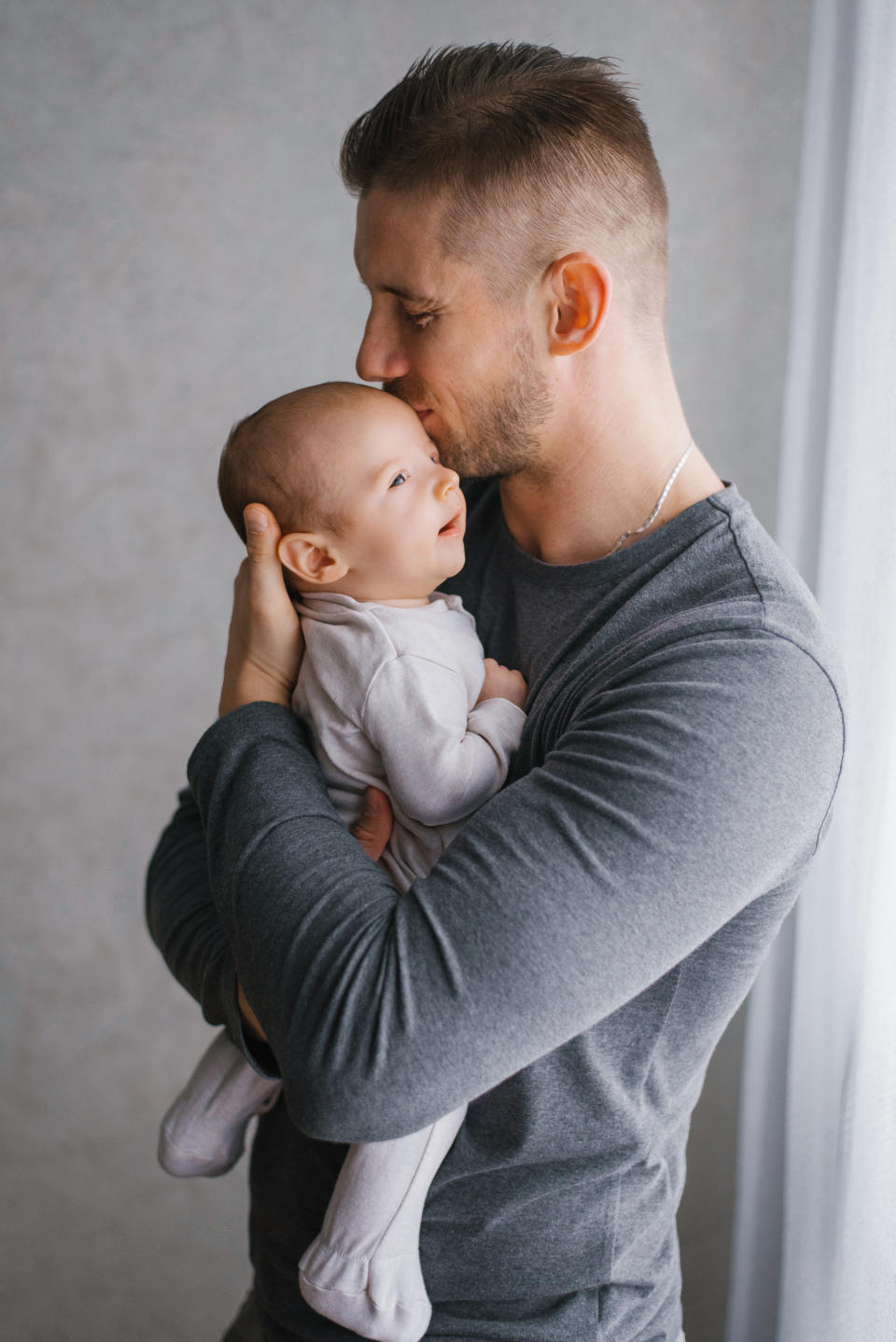 Man embraces and kisses a baby on the forehead. Both are in casual clothing. Names unknown