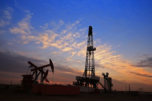A drilling rig near some oil pumps with a nice sunset in the background.