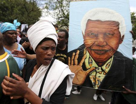 A mourner sings next to a poster former South African President Nelson Mandela outside his residence in Johannesburg December 6, 2013. REUTERS/Siphiwe Sibeko