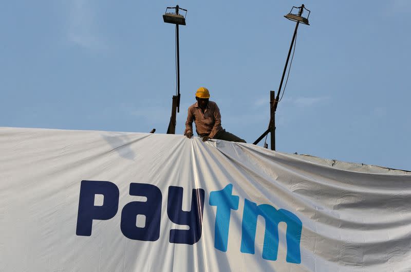 FILE PHOTO: A worker adjusts a hoarding of Paytm, a digital payments firm, in Ahmedabad