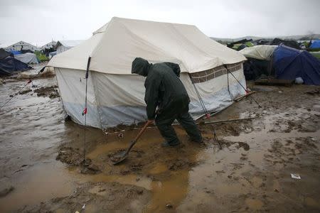 A man shovels mud outside a tent in a flooded field during heavy rainfall at a makeshift camp for refugees and migrants at the Greek-Macedonian border near the village of Idomeni, Greece, May 21, 2016. REUTERS/Kostas Tsironis