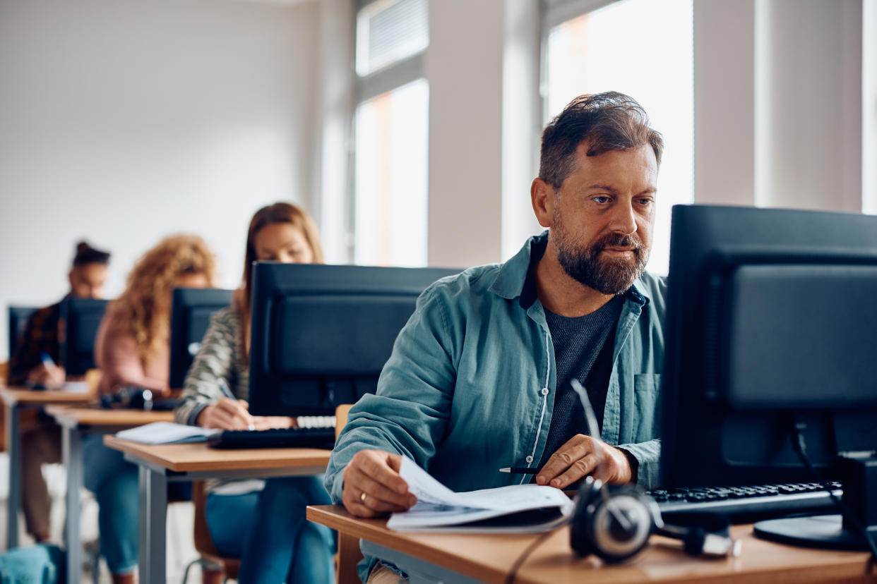 Mature man studying on desktop PC during computer class at university classroom.