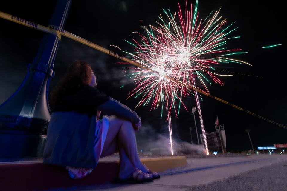 Geri Wade of Stockton sits on a curb to watch the fireworks show Saturday at Stockton Ballpark. Wade watched the fireworks two weeks ago after a hockey game and wanted to see them again.