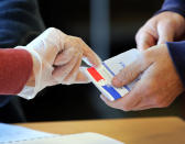 A voting volunteer using gloves during the first round of the municipal elections, in Saint Pee sur Nivelle, southwestern France, Sunday March 15, 2020. France is holding nationwide elections Sunday to choose all of its mayors and other local leaders despite a crackdown on public gatherings because of the new virus. For most people, the new coronavirus causes only mild or moderate symptoms. For some it can cause more severe illness. (AP Photo/Bob Edme)
