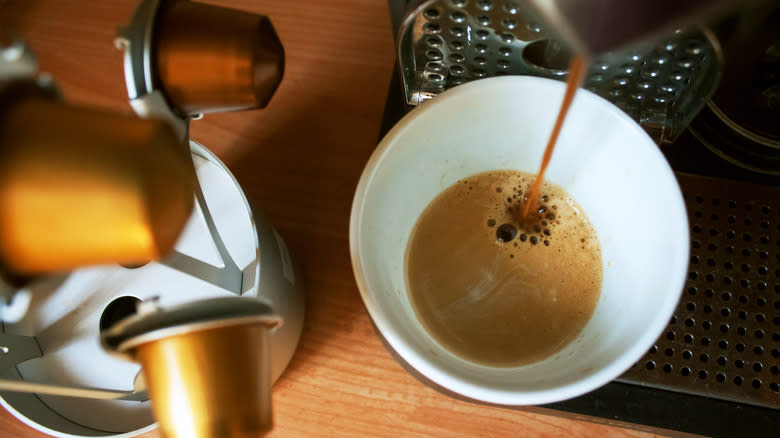 A Nespresso machine pouring a shot of coffee next to a pile of pods