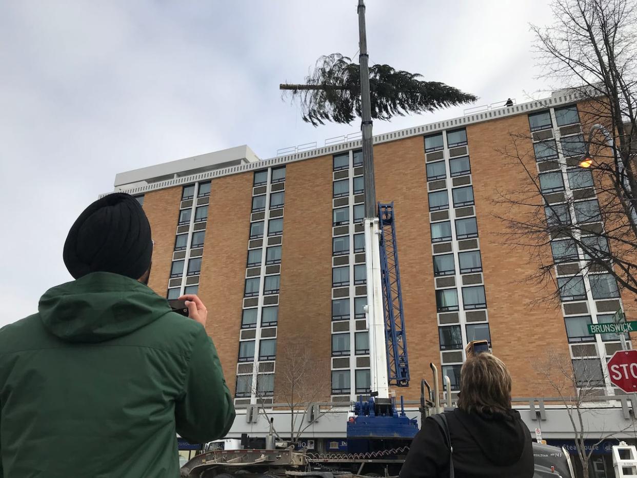 The large Christmas tree is lifted onto the roof of the Coast Prince George Hotel in downtown Prince George in front of onlookers in 2019. (Andrew Kurjata/CBC - image credit)