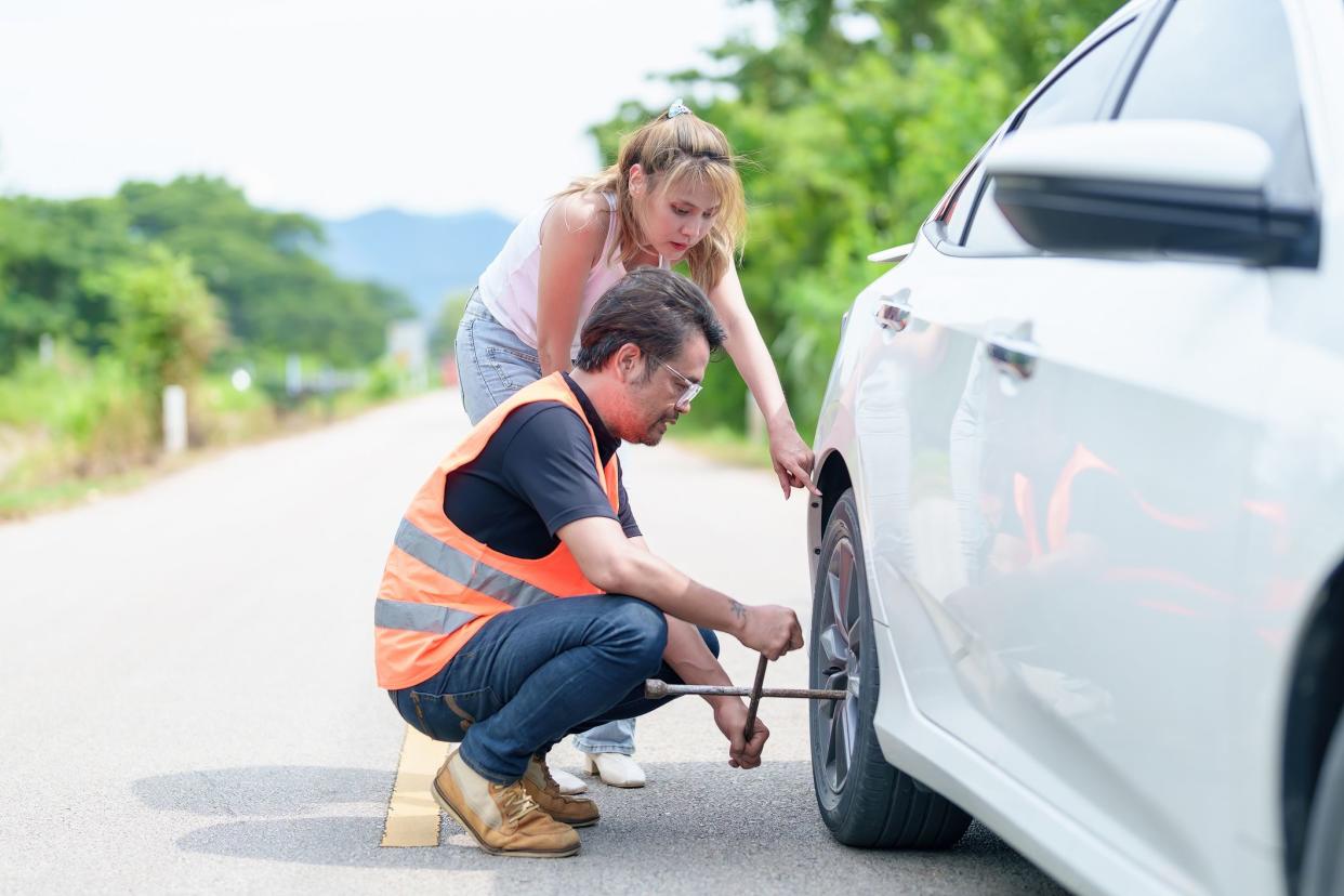 Road assistance worker helping young woman to change a car wheel on the highway