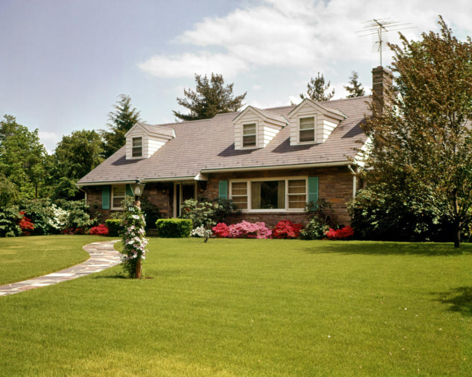 A well-maintained suburban house with a large front lawn, stone pathway, and well-manicured shrubs and flowers