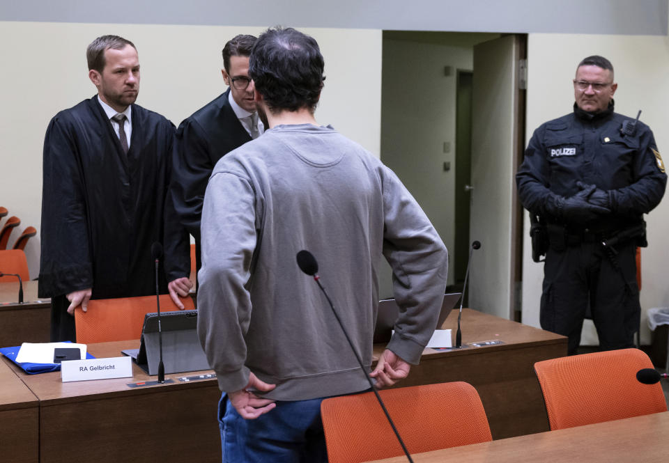 The defendant, front, stands together with his lawyers Martin Gelbricht, rear left, and Maximilian Baer, rear second left, in the courtroom in Munich, Germany, Friday, Dec. 23, 2022. The German court convicted the man of attempted murder and bodily harm and sentenced him to 14 years in prison on Friday over a knife attack on a train last year that left four people wounded. (Sven Hoppe/dpa via AP)