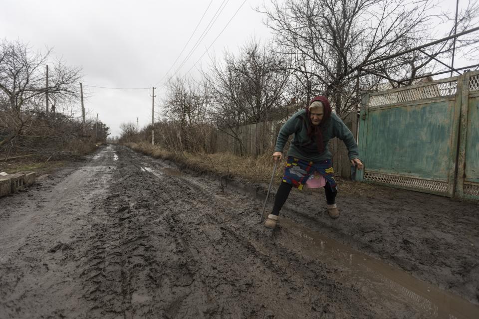 Halyna Moroka tries to cross a bumpy road near her house in the village of Nevelske in eastern Ukraine, Friday, Dec. 10, 2021. The 7-year-old conflict between Russia-backed separatists and Ukrainian forces has all but emptied the village. “We have grown accustomed to the shelling,” said Moroka, 84, who has stayed in Nevelske with her disabled son. (AP Photo/Andriy Dubchak)