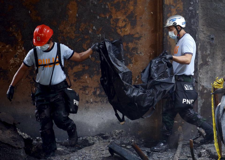 Police carry a body bag containing a charred remains of a worker inside a gutted slipper factory in Valenzuela, Metro Manila in the Philippines May 14, 2015.A fire at a factory making rubber slippers killed 31 workers in the Philippine capital on Wednesday, and dozens were missing and feared dead, officials said. REUTERS/Erik De Castro