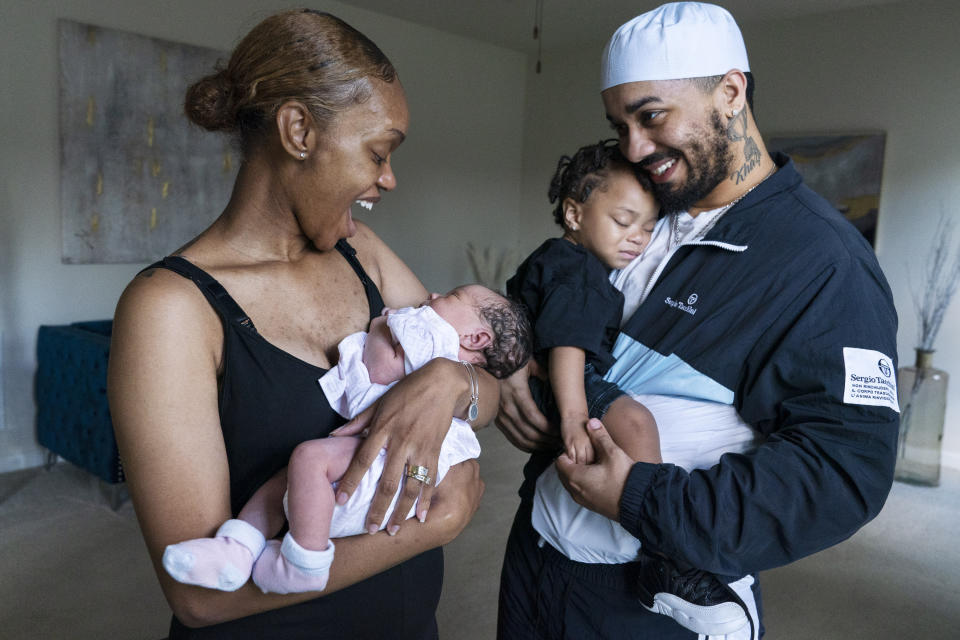Aaliyah Wright, 25, of Washington, reacts on seeing a smile from her newborn daughter Kali, as her husband Kainan Wright, 24, of Washington, holds their son Khaza, 1, during a visit to the children's grandmother in Accokeek, Md., Tuesday, Aug. 9, 2022. A landmark social program is being pioneered in the nation’s capital. Coined “Baby Bonds,” the program is designed to narrow the wealth gap. The program would provide children of the city’s poorest families up to $25,000 when they reach adulthood. (AP Photo/Jacquelyn Martin)