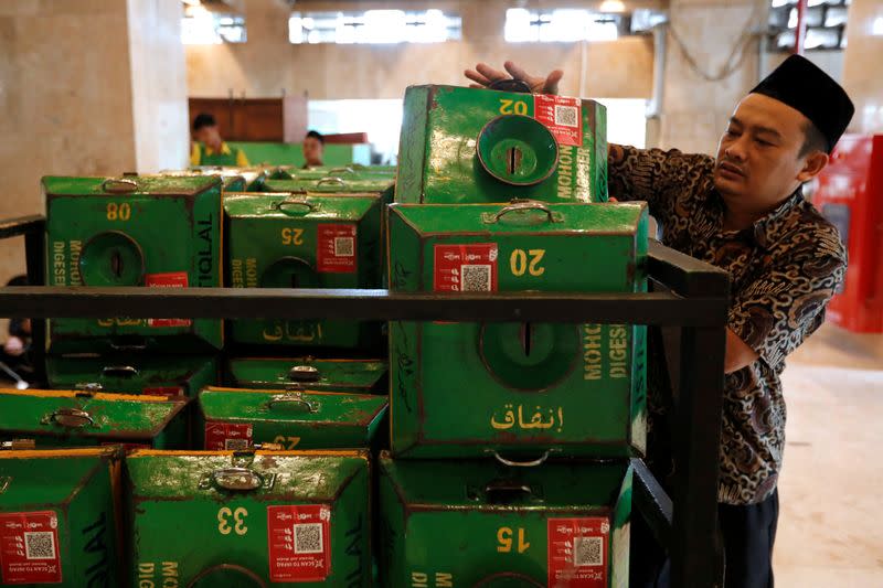 A volunteer collects alms boxes with QR codes and stacks them on a cart after Friday prayers at Istiqlal mosque in Jakarta