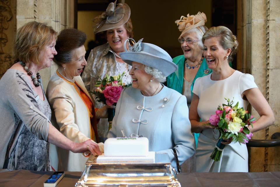 Queen Elizabeth cuts a cake as Sophie, Countess of Wessex, and Princess Anne look on