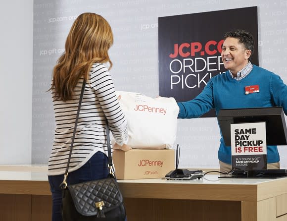 Person picking up packages from clerk behind counter with sign reading JCP.com Order Pickup.