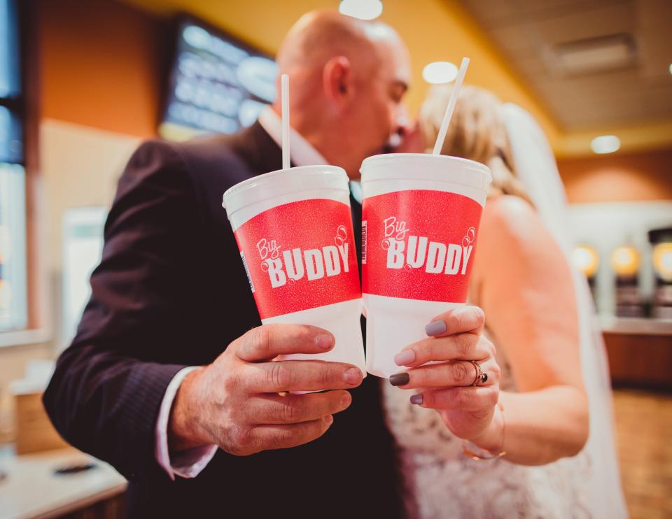 A bride and groom hold large cups that say "Big Buddy."