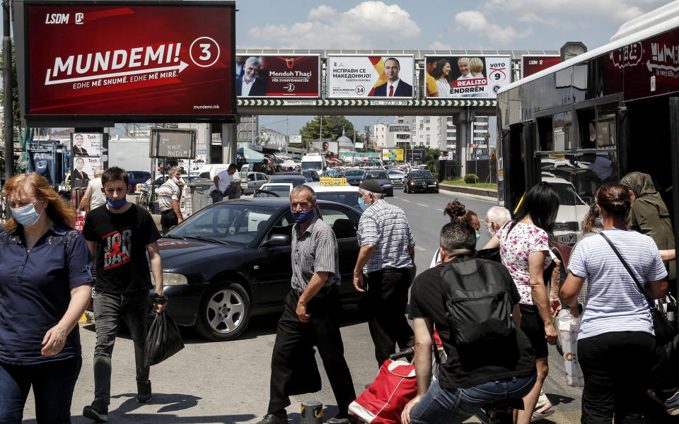People wearing face masks exit a bus as various electoral campaign posters are displayed in a street in Skopje, North Macedonia on Saturday, July 11, 2020. North Macedonia holds its first parliamentary election under its new country name this week, with voters heading to the polls during an alarming spike of coronavirus cases in the small Balkan nation. (AP Photo/Boris Grdanoski)