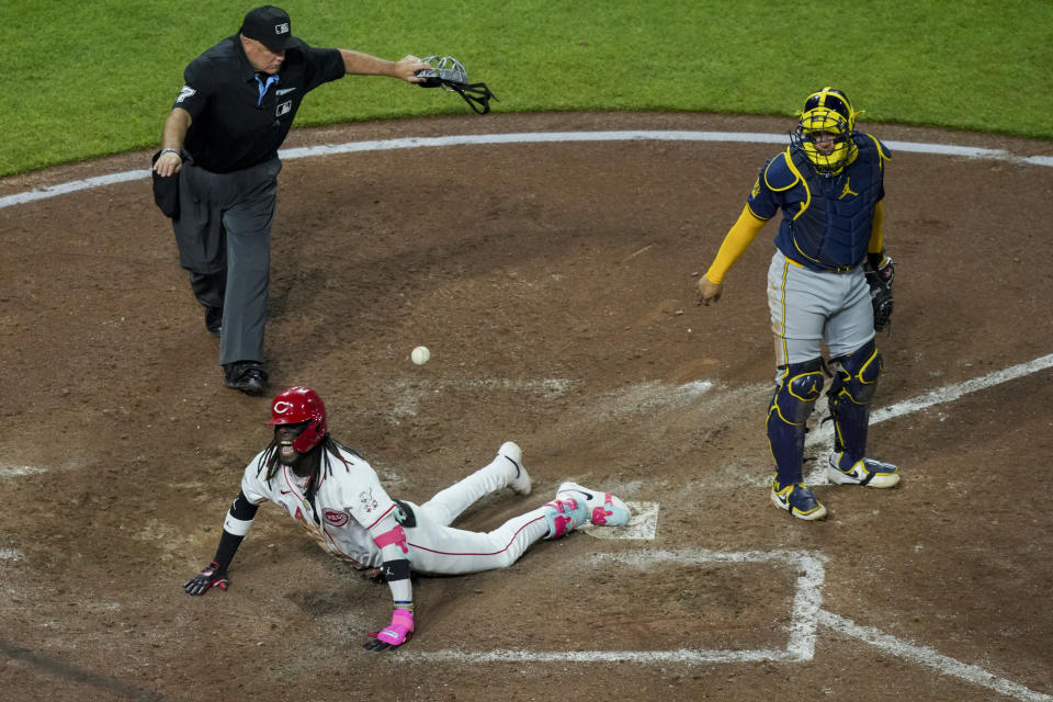 Umpire Brian O'Nora, top left, signals safe as Cincinnati Reds' Elly De La Cruz, bottom center, yells while sliding across home plate after hitting an inside-the-park home run during the seventh inning of a baseball game against the Milwaukee Brewers in Cincinnati, Monday, April 8, 2024. (AP Photo/Aaron Doster)