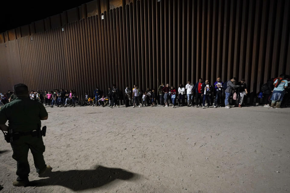 Migrants wait to be processed by Border Patrol agents near the end of a border wall Tuesday, Aug. 23, 2022, near Yuma, Arizona. The Border Patrol is seeing a dramatic shift in the type of migrants who come across the busiest places on the U.S.-Mexico. Migrants are now coming from more than 100 countries, and Mexicans are virtually absent. (AP Photo/Gregory Bull)