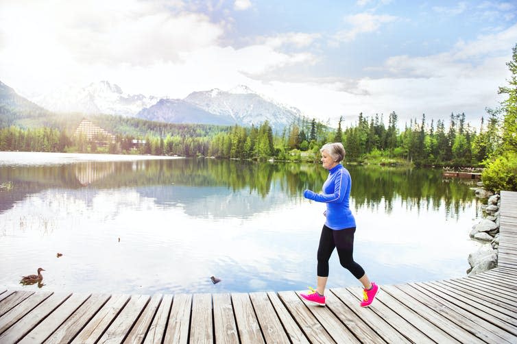 Older woman out for a jog on a pier by a lake.