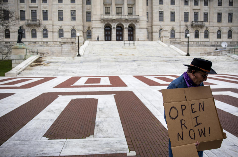 FILE - in this May 1, 2020 file photo, James Dunn stands outside the statehouse in Providence, R.I. with a handmade sign. The smallest U.S. state has the longest name, and it's not sitting well for some in the George Floyd era. Officially, Rhode Island was incorporated as "The State of Rhode Island and Providence Plantations" when it declared statehood in 1790. Now, opponents have revived an on-and-off effort to lop off the plantations reference, saying it evokes the dark legacy of slavery. (AP Photo/David Goldman, File)