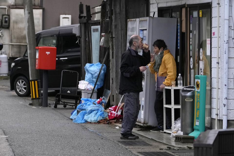People brush their teeth in front of their shop in Wajima in the Noto peninsula facing the Sea of Japan, northwest of Tokyo, Sunday, Jan. 7, 2024. Monday's temblor decimated houses, twisted and scarred roads and scattered boats like toys in the waters, and prompted tsunami warnings. (AP Photo/Hiro Komae)