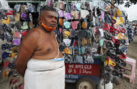 A man wearing a face mask around his chin stands next to a cart displaying face masks for sale in Bengaluru, capital of the southern Indian state of Karnataka, Thursday, Dec. 2, 2021. India on Thursday confirmed its first cases of the omicron coronavirus variant in two men in Karnataka who came from abroad. (AP Photo/Aijaz Rahi)