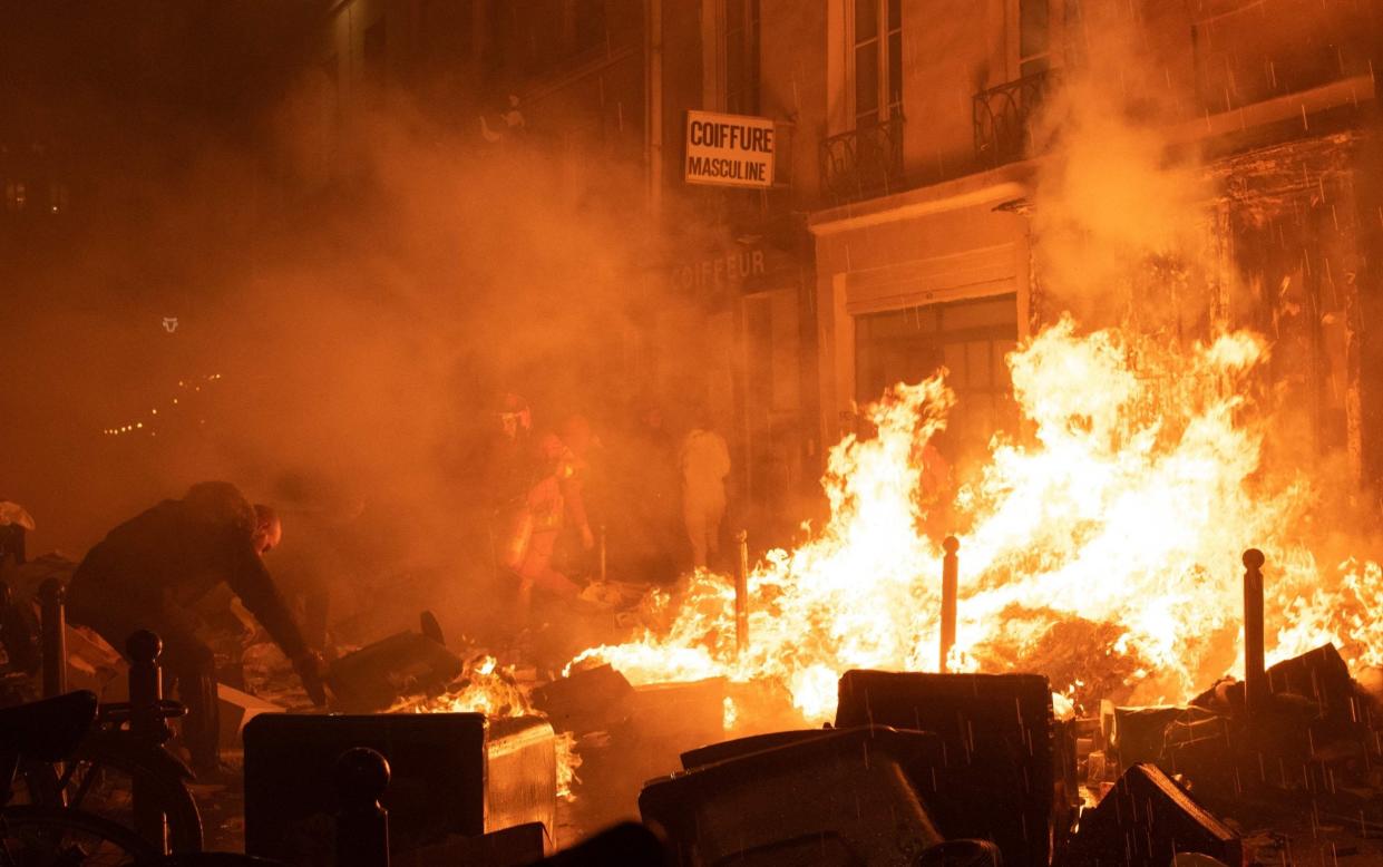 TOPSHOT - A local resident (L) and a firefighter try to extinguish a fire of rubbish during a demonstration, a week after the government pushed a pensions reform through parliament without a vote, using the article 49.3 of the constitution, in Paris on March 23, 2023. - Some 1.089 million protesters took part in demonstrations in France on March 23, 2023, against President Emmanuel Macron's pension reform, the interior ministry said, with 119,000 marching in Paris alone. - ANNA KURTH/AFP