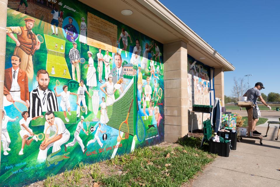 Los visitantes del Kossover Tennis Center pasan por primera vez por un nuevo mural del artista Andy Valdivia.  Se dedicarán más de 500 horas a los dos paneles que cubren el lado este del edificio.