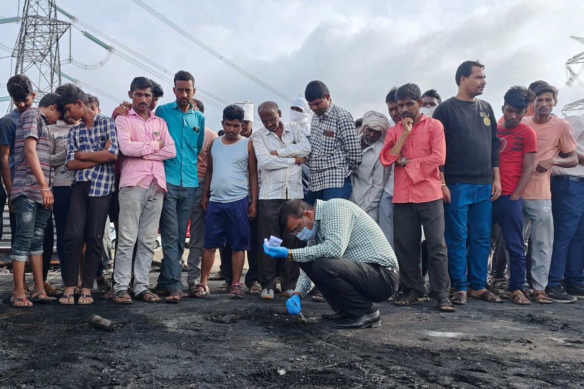 Onlookers stand next to an official collecting samples from the remains of a bus that caught fire along the Samruddhi Expressway (AFP via Getty Images)