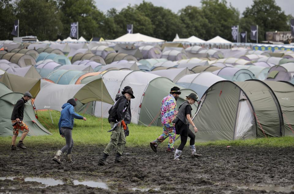 Metal fans walk on the muddy festival grounds ahead of the beginning of the Wacken Open-Air (WOA) Festival, in Wacken, Germany, Tuesday Aug. 1, 2023. WOA Festival takes place from August 2 to August 5, and is considered the largest heavy metal festival in the world. (Christian Charisius/dpa via AP)