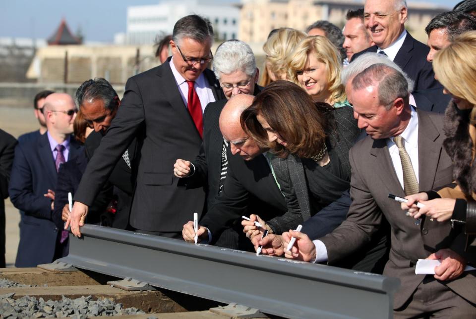 Gov. Jerry Brown, center left, and his wife Anne Gust, fourth from right, sign a portion of the rail at the California High Speed Rail Authority ground breaking event as Gina McCarthy, administrator of the U.S. Environmental Protection Agency, standing next to Brown at left, watches, Tuesday, Jan. 6, 2015 in Fresno, Calif. Gina McCarthy. California’s high-speed rail project has become the first in the nation to break ground. Tuesday’s groundbreaking was attended by several hundred people who gathered near old rail lines in an industrial section of downtown Fresno. (AP Photo/Gary Kazanjian)