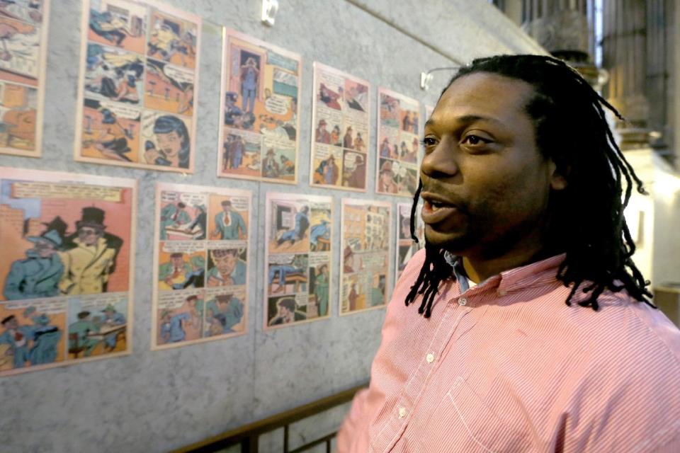 In this Wednesday, Feb. 5, 2014 photo, Chay Tyler stands near the pages from the single issue of “All-Negro Comics” that is part of an exhibit on display at the City/County building in downtown Pittsburgh. The exhibit chronicles some early African American artists and a publisher who started to break the comic color barrier in the 1930s and 1940s. Tyler is a program coordinator for the city Department of Parks and Recreation and helped curate the exhibit. (AP Photo/Keith Srakocic)