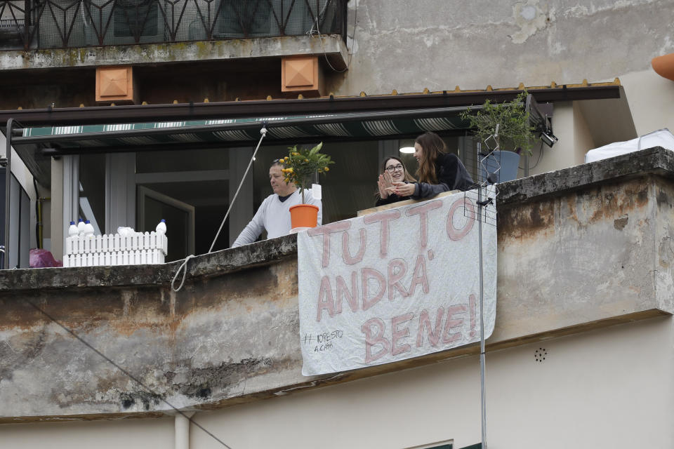 In this photo taken on Saturday, March 14, 2020, people stand by a banner reading "Everything will be alright", at the Garbatella neighborhoodin Rome. The nationwide lockdown to slow coronavirus is still early days for much of Italy, but Italians are already are showing signs of solidarity. This week, children’s drawings of rainbows are appearing all over social media as well as on balconies and windows in major cities ready, ‘’Andra’ tutto bene,’’ Italian for ‘’Everything will be alright.’’ For most people, the new coronavirus causes only mild or moderate symptoms. For some, it can cause more severe illness, especially in older adults and people with existing health problems. (AP Photo/Alessandra Tarantino)