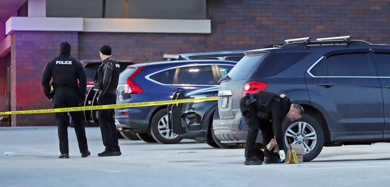 An Akron Police officer gathers evidence from the parking lot after a shooting injured two men at the Newcomer Funeral Home in Akron Friday.