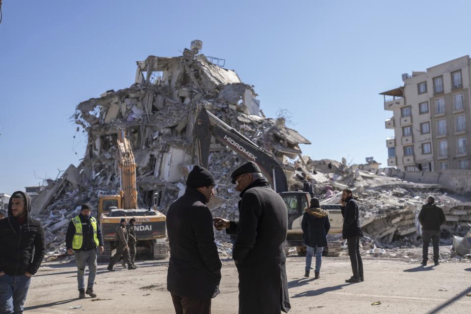 Local residents stand in front of a destroyed building in Nurdagi, southeastern Turkey, Thursday, Feb. 9, 2023. Thousands who lost their homes in a catastrophic earthquake huddled around campfires and clamored for food and water in the bitter cold, three days after the temblor and series of aftershocks hit Turkey and Syria. (AP Photo/Petros Giannakouris)