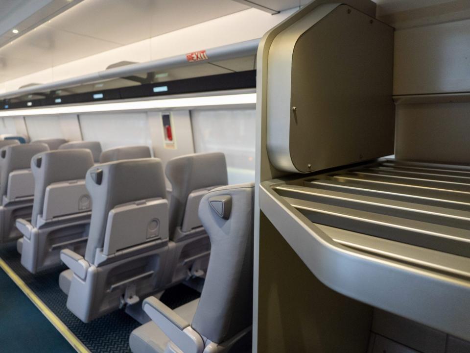 A luggage storage area near rows of seats inside the new Amtrak Acela.