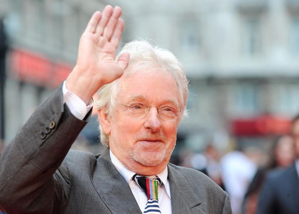 hugh hudson attends the chariots of fire uk film premiere at empire leicester square, waving to crowds in a grey suit