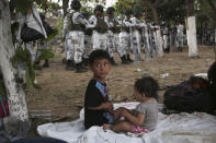 Con una línea de guardias nacionales mexicanos al fondo, dos niños migrantes acampan en la orilla mexicana del río Suchiate, en la frontera con Guatemala, cerca de Ciudad Higalgo, México, el lunes 20 de enero de 2020. (AP Foto/Marco Ugarte)