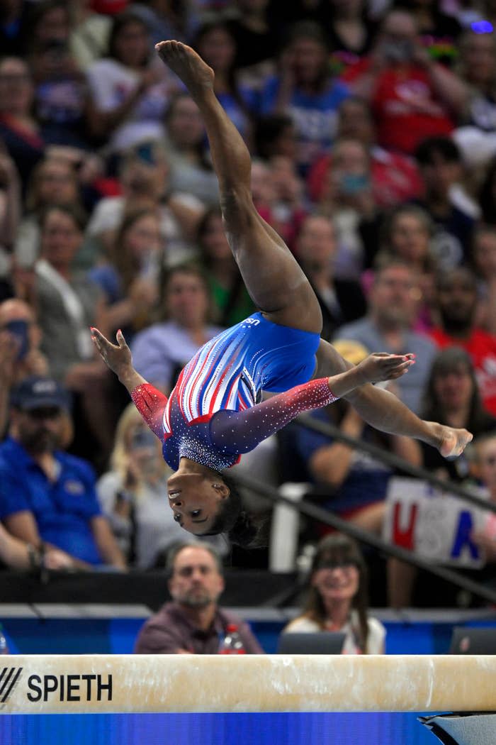 Simone Biles performs a flip on the balance beam during a gymnastics competition, wearing a star-covered leotard