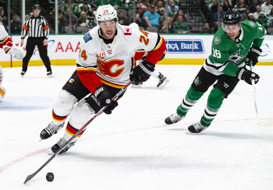 Calgary Flames defenseman Travis Hamonic (24) skates with the puck as Dallas Stars center Joe Pavelski (16) pursues during the first period of an NHL hockey game, Sunday, Dec. 22, 2019, in Dallas. (AP Photo/Sam Hodde)