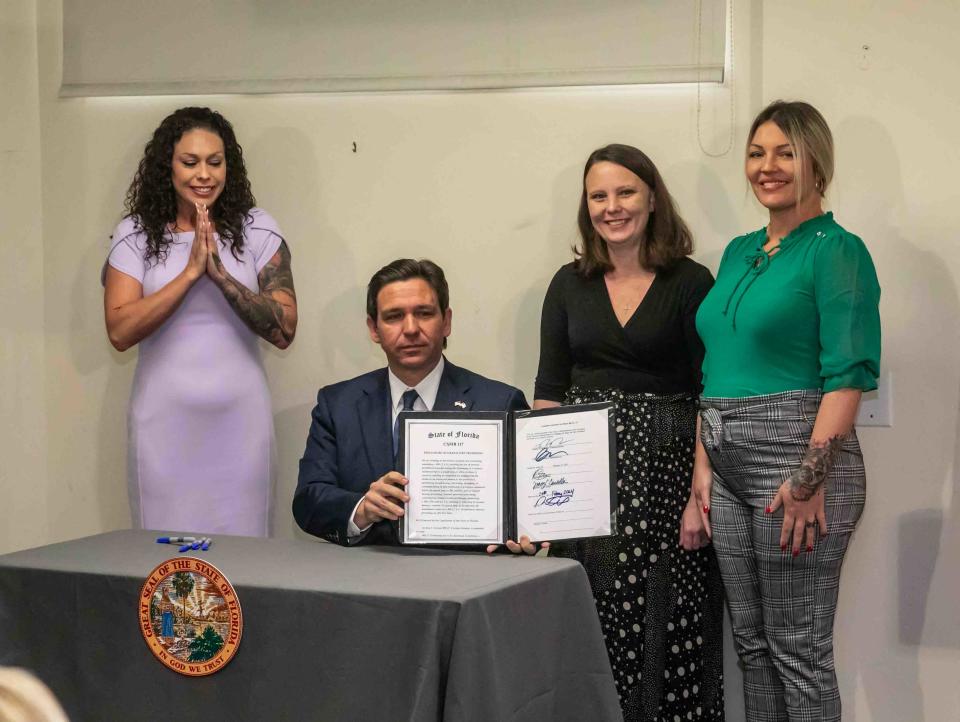 Gov. Ron DeSantis holds up a bill meant to release records from a 2006 Jeffrey Epstein grand jury inside the Palm Beach Police Department on Thursday, Feb. 29. Participating in the proceedings were several Epstein victims including, from left, Hayley Robson, Jena-Lisa Jones, and Courtney Wild.