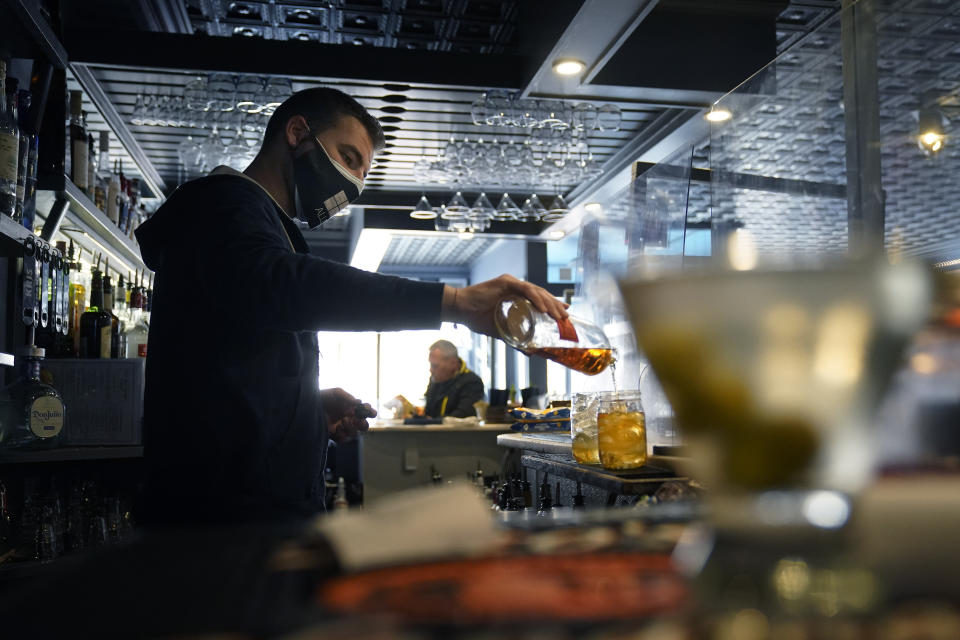 Bartender Denis Angelov, of Provincetown, Mass., pours drinks at Tin Pan Alley restaurant, Tuesday, April 6, 2021, in Provincetown. Hotels, restaurants and other businesses in tourist destinations are warning that hiring challenges during the coronavirus pandemic could force them to pare back operating hours or curtail services just as they’re eyeing a bounce-back summer. (AP Photo/Steven Senne)